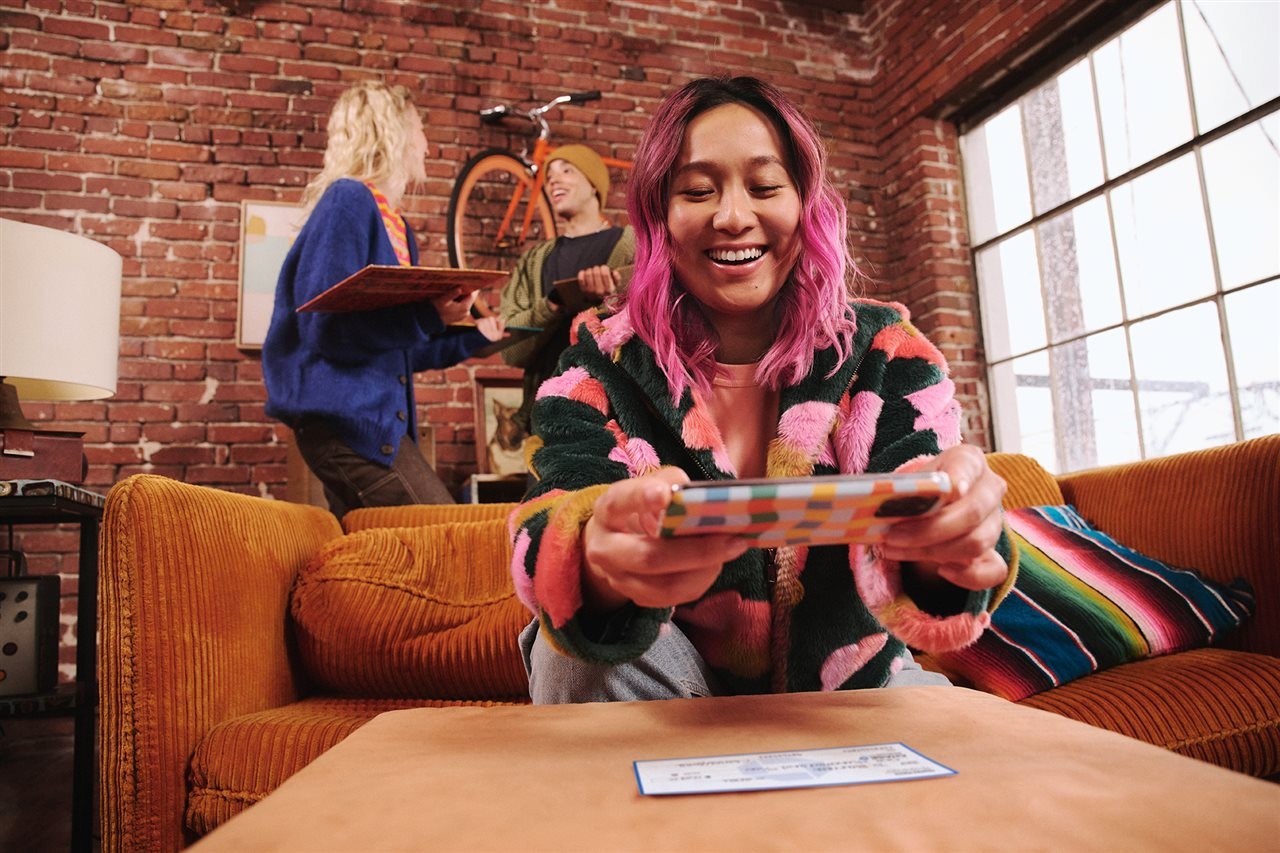 College student using an app on her phone to deposit a check while sitting on a couch in her dorm room.